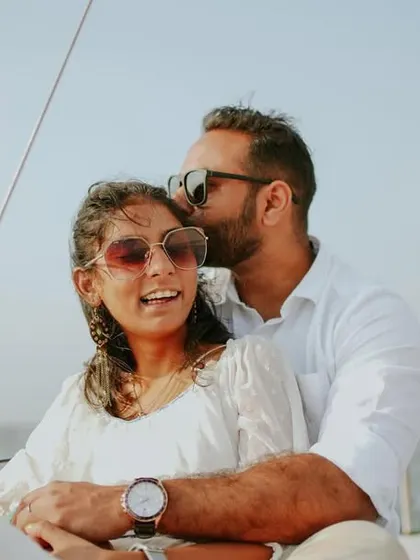 A sweet and sunny moment from a pre-wedding yacht shoot, with the groom-to-be kissing his partner's cheek as she smiles.