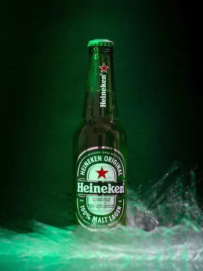 A bottle of Heineken beer is captured with a creative splash of water around its base. This dynamic product shot uses motion and dramatic green lighting to create an exciting image.