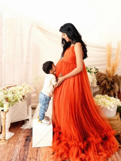 A sweet kiss for the baby bump from the soon-to-be big brother. This heartwarming photo in a flowing orange gown captures the love and excitement of a growing family.