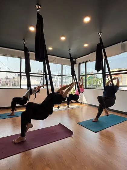A group of students stretching in their hammocks. The large windows in our studio provide a beautiful, light-filled backdrop for our aerial classes.