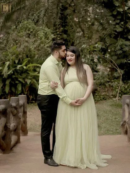 A tender kiss on the forehead during an outdoor session. The couple is coordinated in soft green tones, blending beautifully with the park's foliage.