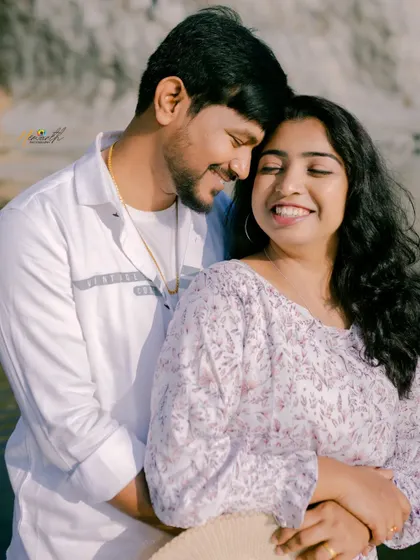 A bright, happy close-up of a couple embracing by the water. Their genuine smiles are the focus of this warm and sunny portrait.