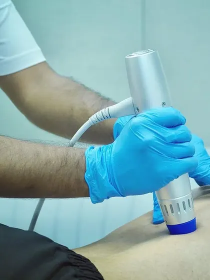A therapist uses a shockwave therapy device on a client's leg. This advanced modality helps accelerate recovery from injuries by stimulating the body's natural healing processes.
