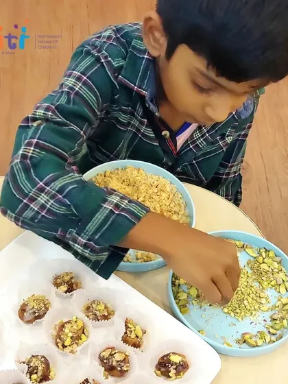 A child sprinkles crushed pistachios on the finished date desserts. This final touch adds texture and flavor, completing the culinary creation.