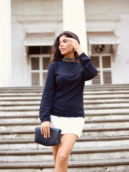 Modeling a "Femme Fatale" look with a collared black top and white mini skirt on city steps, creating a chic and powerful urban aesthetic.