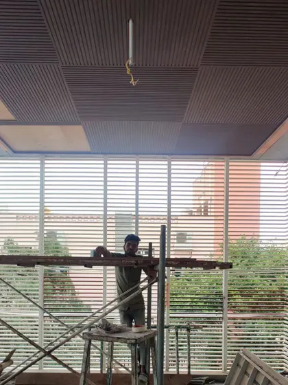 A view of a ceiling with a patterned wood finish, with a worker on scaffolding installing the surrounding louvered screens.