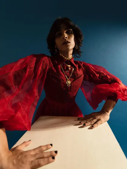 A dramatic, wide-angle shot for Amama Jewels. The pose, bold red attire, and high-contrast lighting create a powerful image that showcases the statement jewelry.
