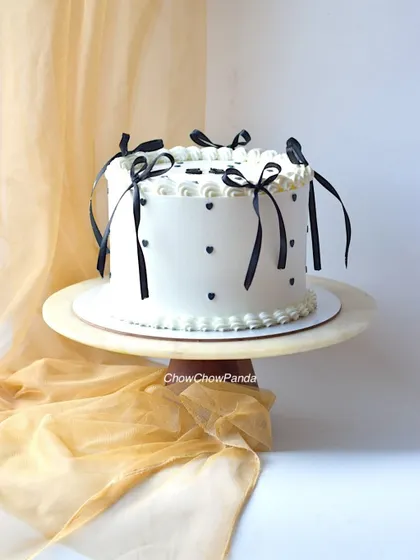 For a touch of classic elegance, I created this vintage-style cake. It has a clean white buttercream finish, decorated with simple black hearts and delicate black ribbons, offering a timeless and chic look for any celebration.