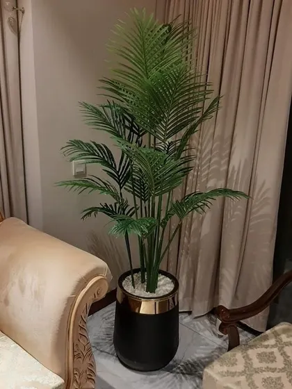 An elegant artificial areca palm in a decorative black and gold pot, placed in a living room corner. It adds a touch of tropical sophistication to the home decor.