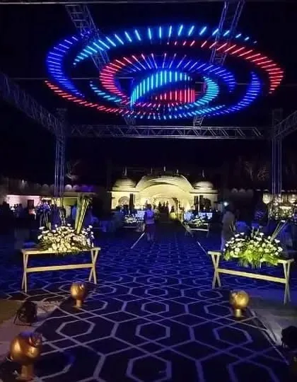 A spectacular overhead lighting rig with swirling red and blue lights, designed to create a dynamic and club-like atmosphere for a Sangeet night.