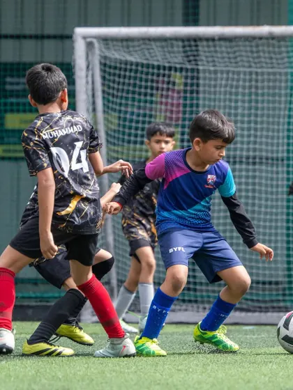 A young player skillfully dribbling the ball under pressure from an opponent. Match situations like these build confidence and decision-making skills.