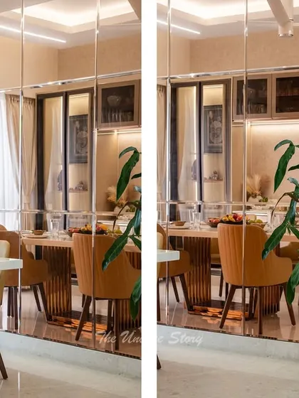 The use of a full-height mirror wall in this dining area doubles the visual space and reflects the elegant setting. It enhances the ambient light from the modern ring chandeliers, creating a bright and sophisticated dining experience.
