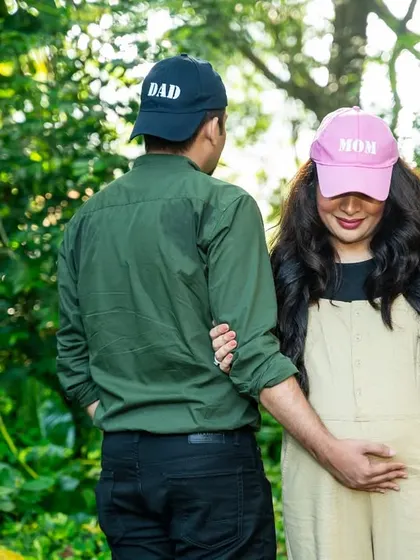 A playful take on the "Mom" and "Dad" caps, with the couple looking away. This candid-style shot adds a bit of mystery and fun to their outdoor maternity session.