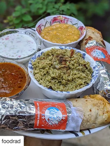 This is what a meal from my cook house looks like when served at home. You can see the rich biriyani rice, bowls of spicy salan and fresh raita, and our foil-wrapped rolls, ready to be enjoyed. It’s a taste of tradition, delivered right to you.