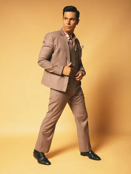 A full-length studio portrait of Randeep Hooda. His confident stance and sharp suit against the warm, neutral background create a timeless and powerful celebrity portrait.