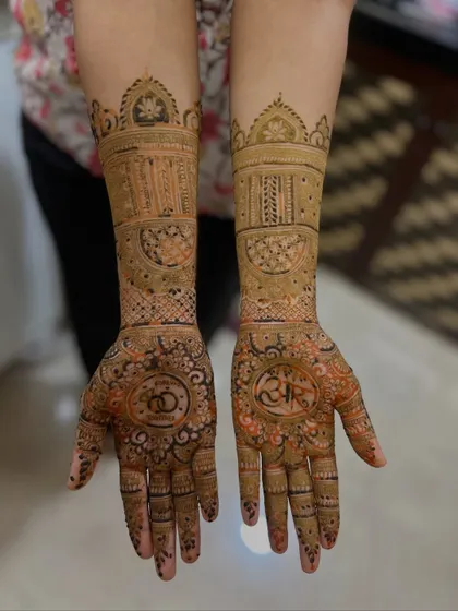 This engagement mehendi features the couple's initials and intertwined rings on the palms. The design continues up the arms with detailed bands and traditional Indian architectural motifs.