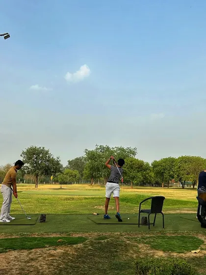 A wide shot of the range on a clear day, with golfers practicing their long game.