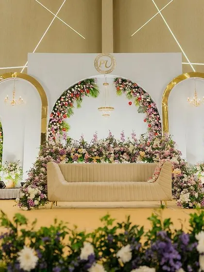 A minimalist yet grand stage featuring three golden arches against a pristine white backdrop. The floral decor is focused and elegant, creating a balanced and contemporary look for a modern reception.