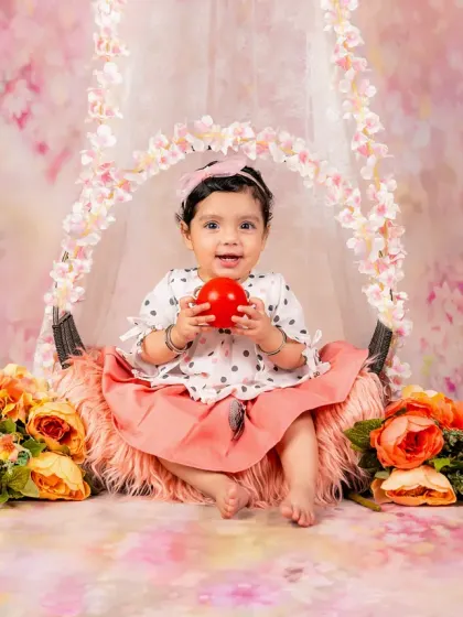 This baby girl is all smiles as she sits in a floral swing, holding a toy. A perfect picture of happiness.