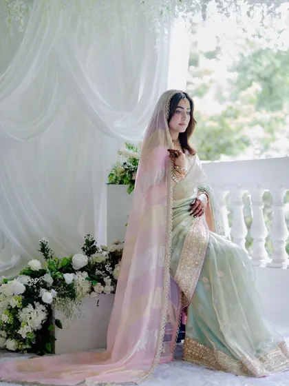 The bride seated by a classic white balustrade, with lush floral arrangements and soft drapes creating a timeless and romantic scene.