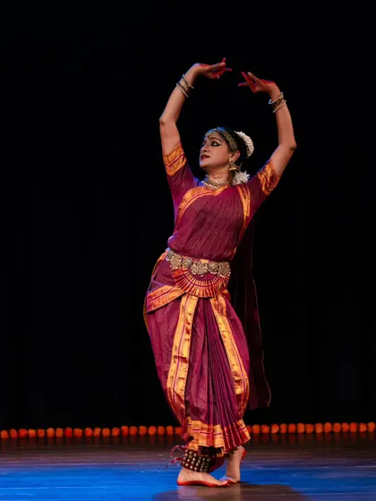 A dynamic pose from a solo recital, capturing the dancer in a moment of fluid motion. The arms are raised in a gesture of offering or celebration.