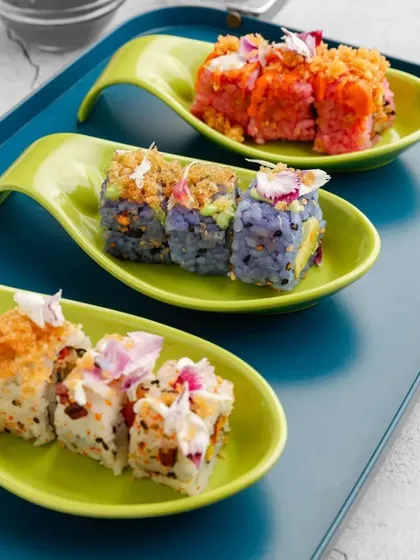 An assortment of our creative vegetarian sushi, including white, pink, and blue rice varieties. Plated on a modern blue tray, this showcases the vibrant and artistic side of our catering.