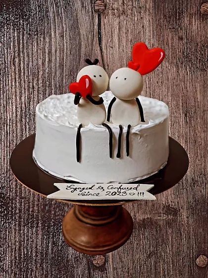 A cute and quirky engagement cake with stick-figure toppers and a playful banner reading "Engaged & Confused".