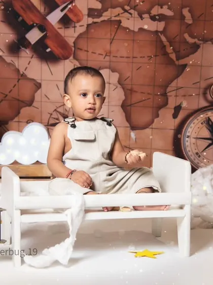 This little aviator is ready to fly, sitting on a miniature bed surrounded by clouds and vintage airplane props.