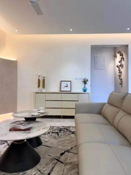 Another view of this modern living room, focusing on the plush sofa, nested marble coffee tables, and sculptural wall art. The ambient lighting from the curved wall adds a soft, warm glow.