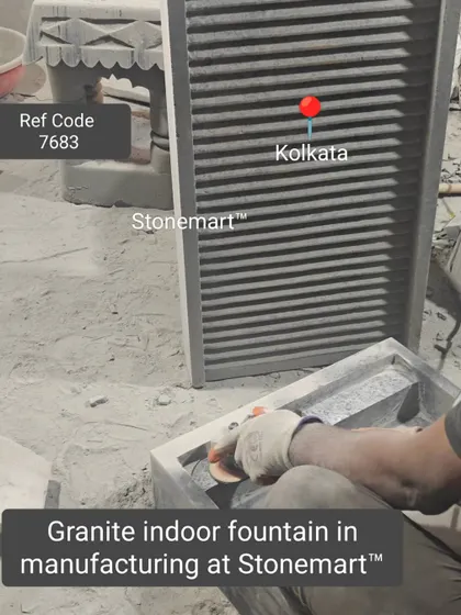 An artisan uses a grinder to smooth the edges of a granite indoor fountain during manufacturing.