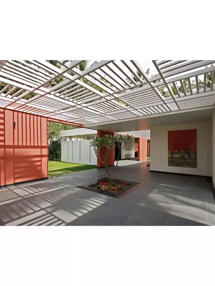 A shaded walkway at the Akriti Experience Centre, where a slatted pergola casts rhythmic shadows on the ground. The interplay of light, shadow, and bold color walls creates a dynamic and constantly changing sensory experience.