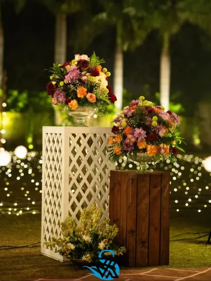 Floral arrangements on display pedestals, with a backdrop of fairy lights. This is a simple way we add magic and light to an outdoor evening event.