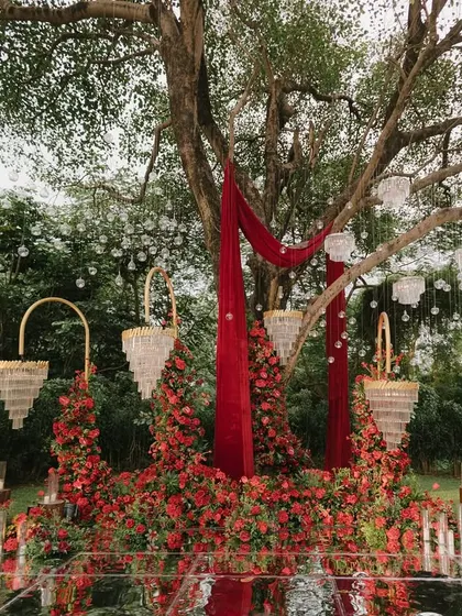 The decor elements coming together under a large tree, with red drapes, chandeliers, and floral towers creating a magical setting.