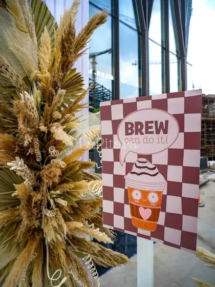 A quirky and motivational sign reading "Brew can do it!" placed alongside rustic dried floral arrangements. These playful elements add character and fun to the corporate environment.