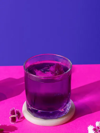 A simple yet striking purple cocktail with an edible flower, using a bold pink and purple background to make the color stand out.