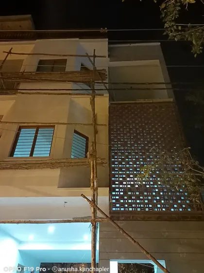 Work in progress on the facade, showing the installation of a decorative jali screen next to the plain exterior wall. This demonstrates how different textures are layered during the execution phase.