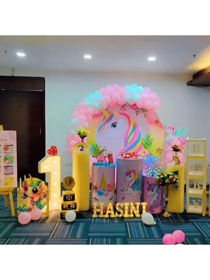 A whimsical unicorn-themed first birthday for Hasini. This decor includes a large unicorn backdrop, a milestone board showing her first year, and soft pastel colors throughout.