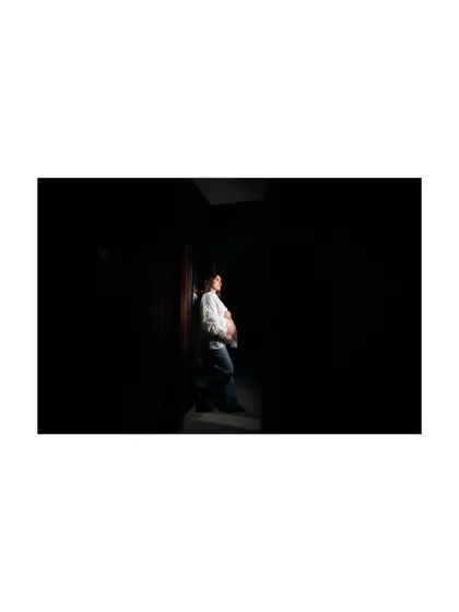 A powerful, low-key lighting portrait where the mom-to-be is highlighted against a dark background. This artistic shot emphasizes the silhouette of her baby bump.