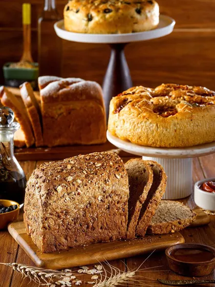 A stunning display of different types of artisan breads and cakes on wooden boards and cake stands. This image captures the variety and craftsmanship of a bakery's offerings in one abundant shot.