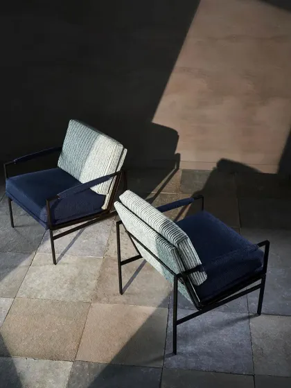 An artistic shot focusing on the form and texture of upholstered chairs. The high angle and strong directional light create dramatic shadows, emphasizing the clean lines and fabric quality.