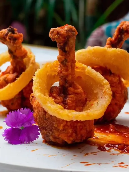 A modern and artistic presentation of our chicken lollipops, served with a crispy onion ring. It's a playful take on a classic appetizer.
