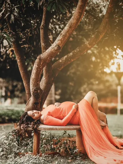 A serene outdoor maternity portrait. The flowing orange gown and natural setting are paired with soft, romantic makeup to create a truly beautiful and artistic memory.
