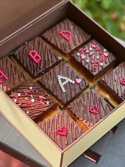 We offer personalized dessert bars for client gifting. This box of our Millionaire Shortbread bars was customized with initials and heart designs, adding a personal touch to a corporate gift.