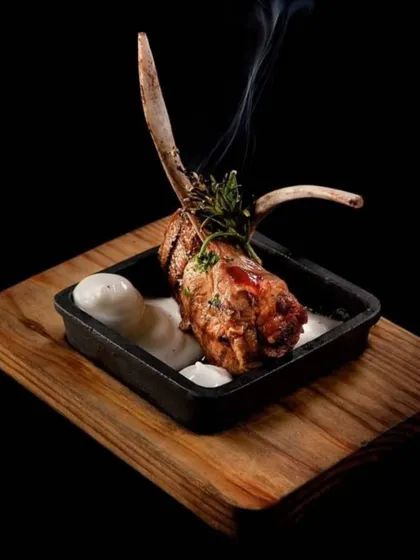 A single, perfectly cooked lamb chop, presented with a dollop of creamy sauce. The smoke rising from the dish hints at the rich, grilled flavour within.