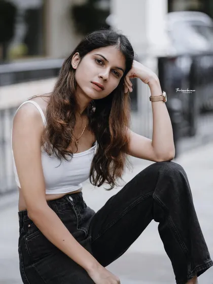A thoughtful and relaxed pose in an urban setting. The simple white top and black jeans create a timeless, casual look.