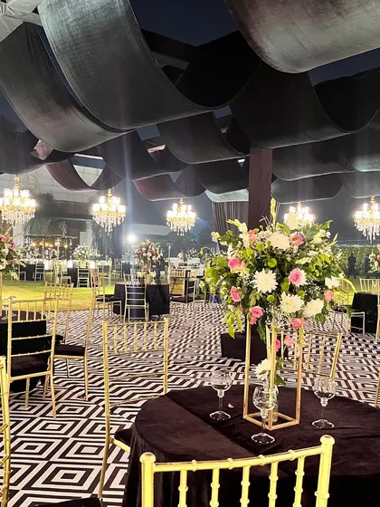 A modern and chic reception setup. The guest tables are covered in black velvet, with gold chairs, set on a bold black and white geometric floor, creating a high-contrast, contemporary look.