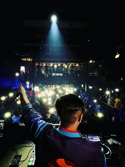 Pointing to the crowd under the spotlight. This is a moment of connection, acknowledging the people who bring the energy to the dance floor.
