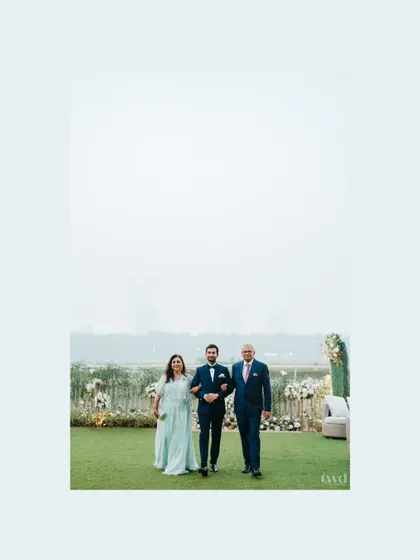 The groom makes his grand entrance, walking down the aisle flanked by his proud parents. A moment of family love and support.