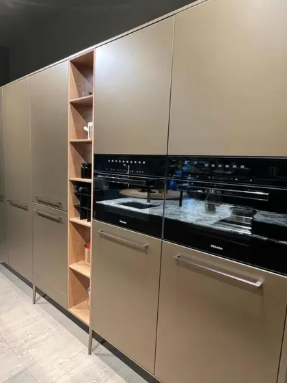 This image showcases a tall unit with integrated ovens and handleless cabinets in a sophisticated beige finish. The slim open shelving in the middle breaks the monotony and adds a display area.