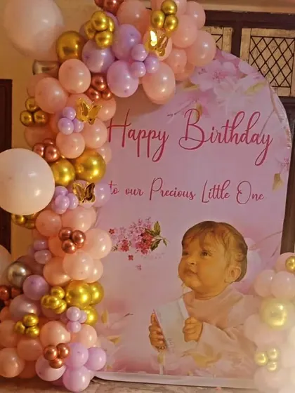 A beautiful custom backdrop for a baby girl's birthday with a pink and gold balloon arch.